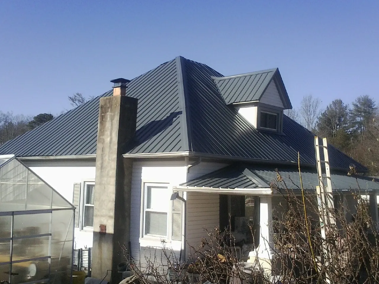 Dark blue standing seam metal roof on a white farmhouse with dormer — Slate & Tile Roof Repair by Roofing Brothers in Atlasburg