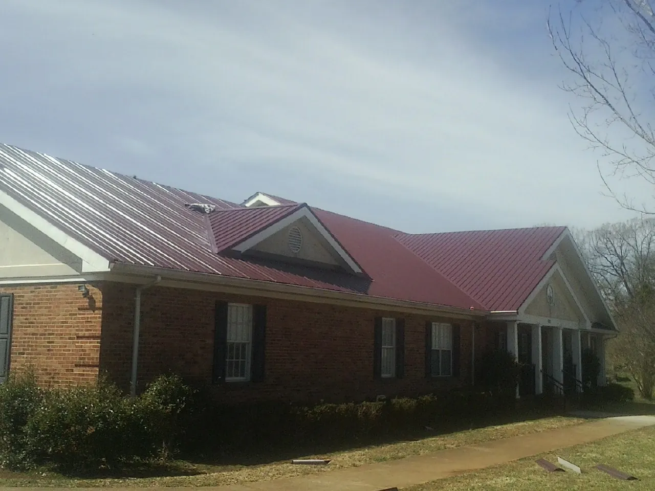Red metal roof with gabled entries on a long brick building, from a Hail Damage Roof Repair job in Atlasburg