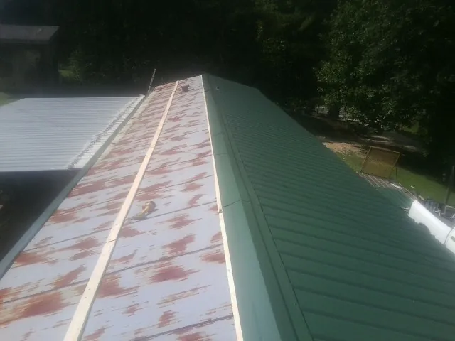 Old rusted panels beside newly installed green metal roofing — Wind Damage Roof Repair by Roofing Brothers in Atlasburg