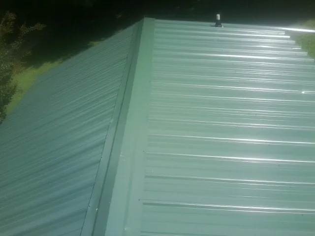 New green metal panels meeting at the ridge of a roof — Flat Roof Repair work by our crew in Atlasburg
