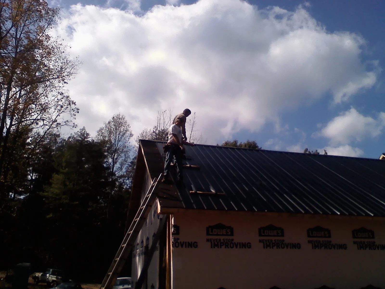 Roofer fastening dark metal panels high against a cloudy sky, from a Roof Inspection job in Atlasburg