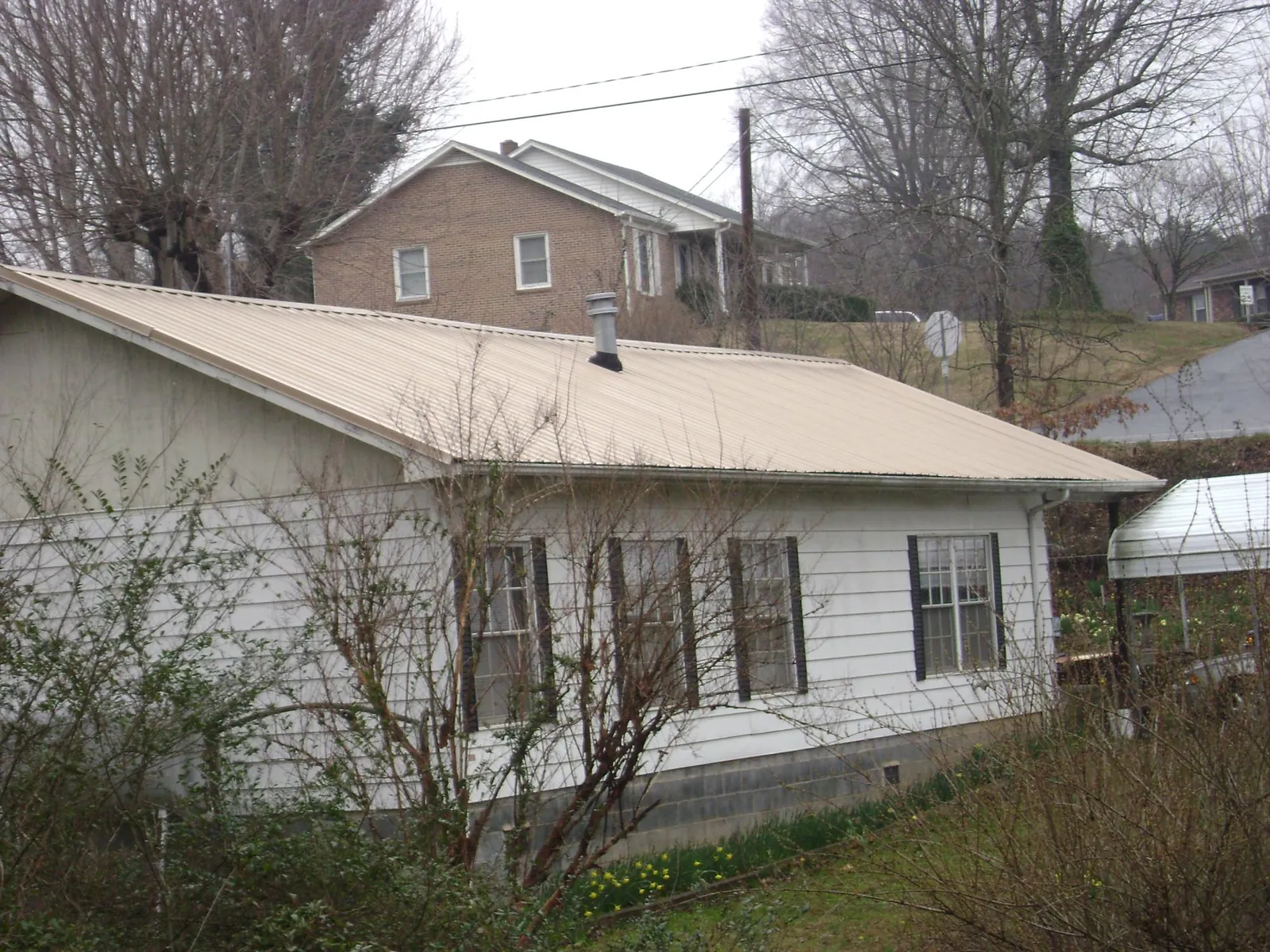 Tan metal roof on a white sided house set into a hillside — Commercial Roofing by Roofing Brothers in Atlasburg